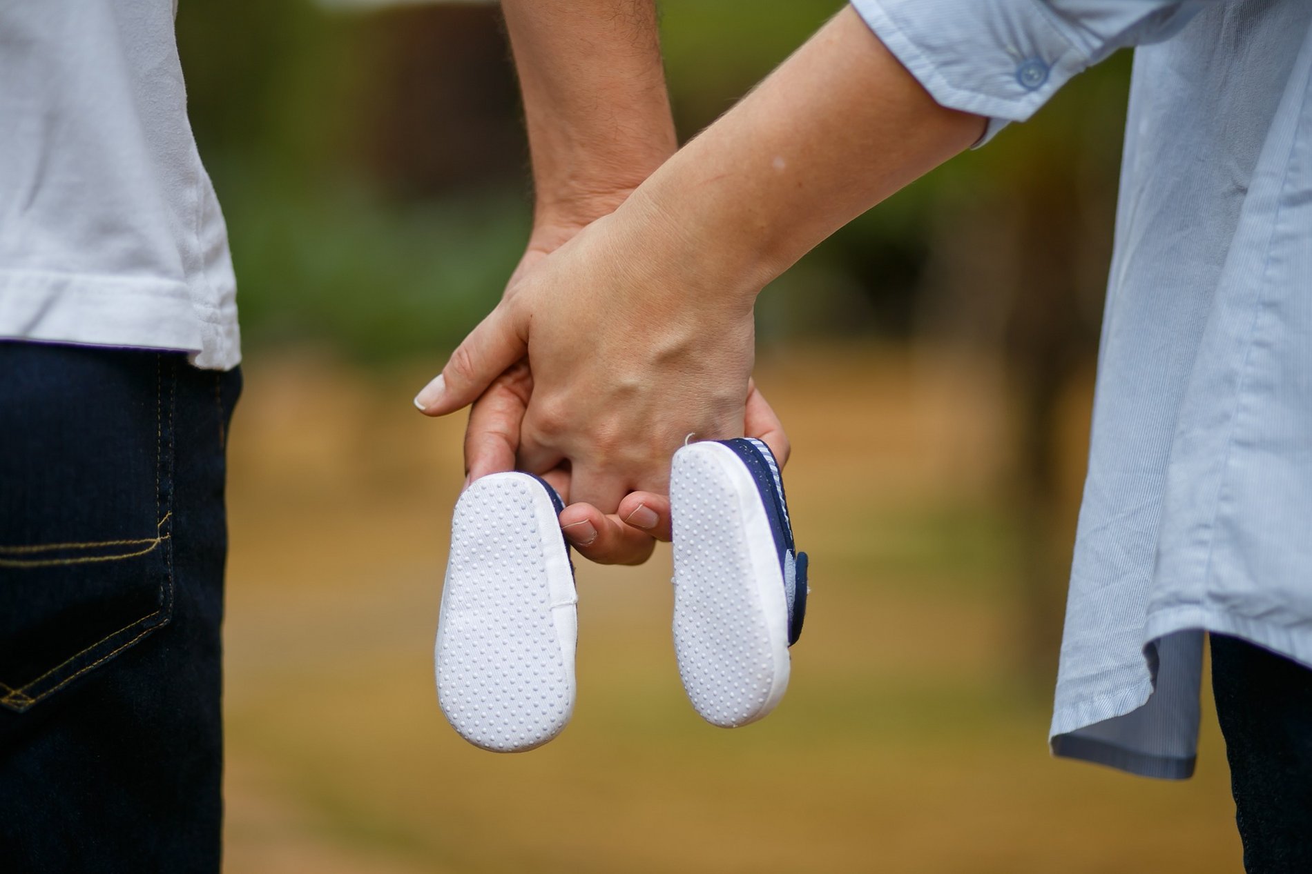 Das Symbolbild zeigt zwei junge Eltern händchenhaltend mit Kinderschuhen