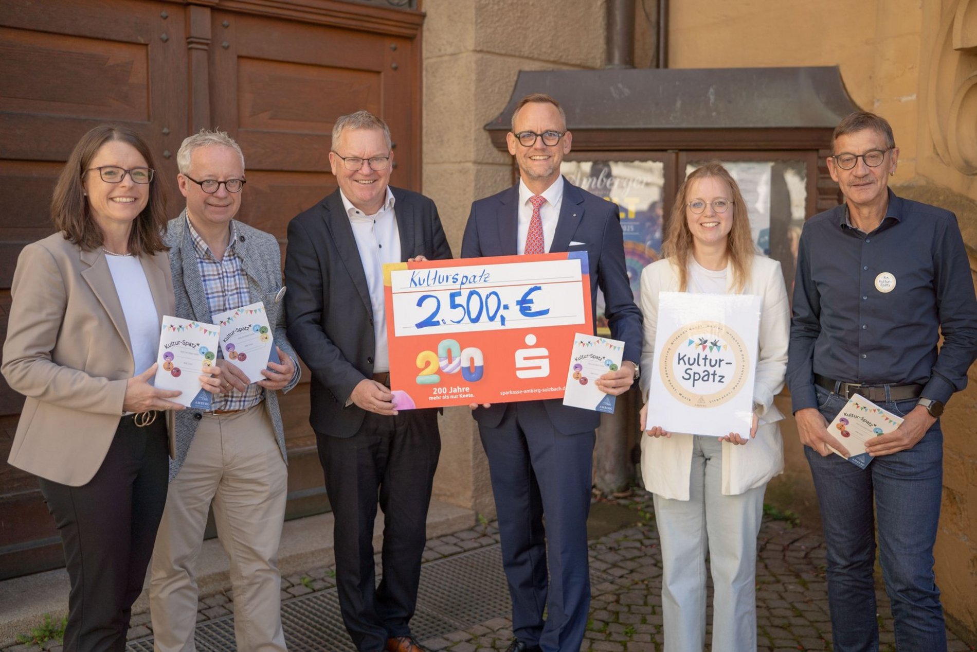 Viele Leute halten einen symbolischen Scheck über 2.500 Euro hoch. 