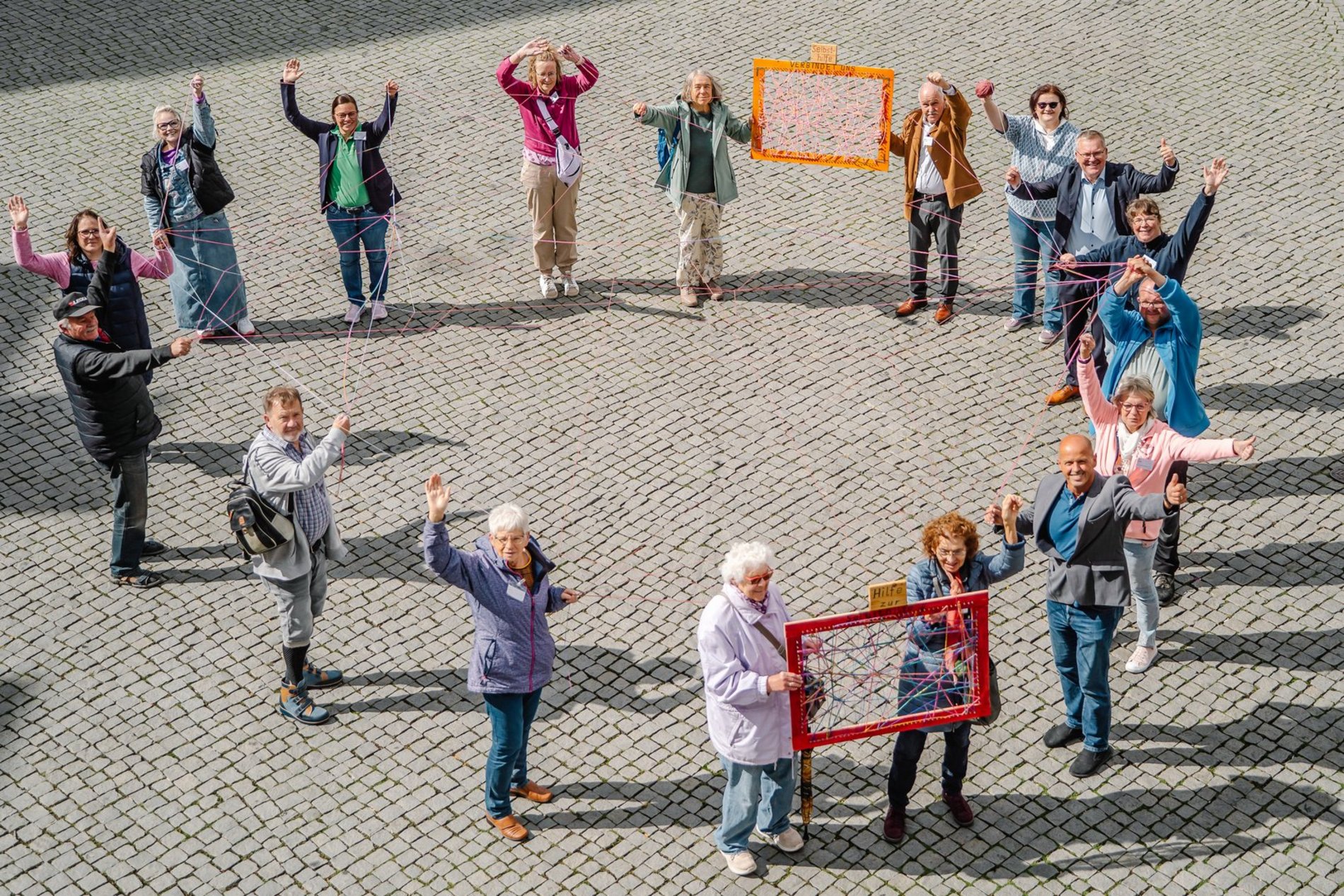 verschiedene Menschen stehen im Kreis und haben ein Netz aus Wolle gesponnen.
